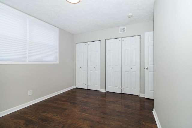 unfurnished bedroom featuring baseboards, dark wood-style floors, visible vents, and multiple closets