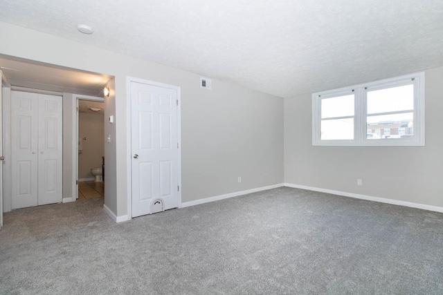 carpeted spare room with baseboards, visible vents, and a textured ceiling