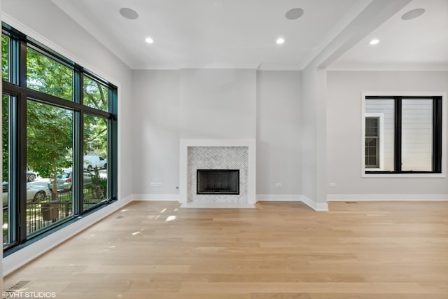 unfurnished living room with a tile fireplace, plenty of natural light, light wood-style flooring, and baseboards