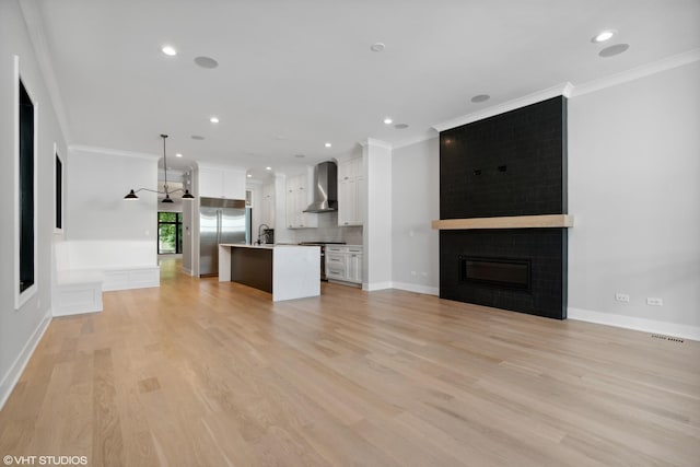 unfurnished living room featuring light wood-style flooring, a large fireplace, a sink, visible vents, and ornamental molding