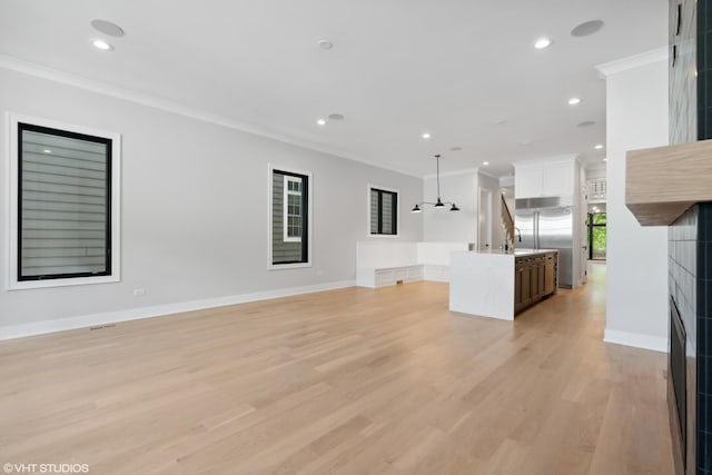 unfurnished living room with baseboards, light wood-style flooring, crown molding, a sink, and recessed lighting