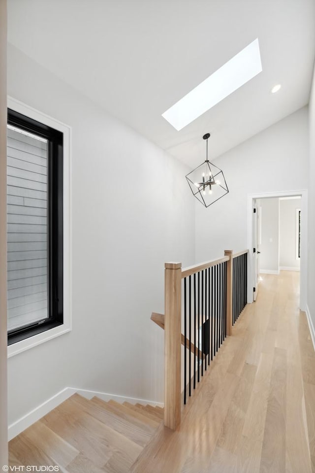 hallway featuring a chandelier, wood finished floors, an upstairs landing, baseboards, and lofted ceiling with skylight