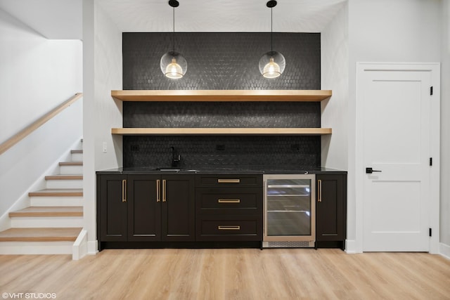 bar with light wood-style flooring, stairway, a sink, wet bar, and beverage cooler