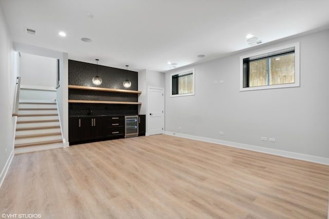 unfurnished living room featuring beverage cooler, visible vents, baseboards, stairway, and light wood-type flooring