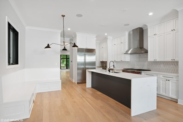 kitchen featuring light wood-style floors, appliances with stainless steel finishes, light countertops, wall chimney range hood, and a sink