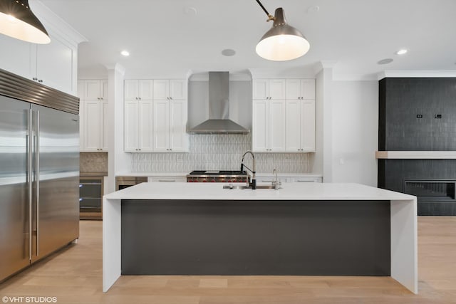 kitchen featuring a sink, white cabinets, light countertops, wall chimney range hood, and stainless steel built in fridge