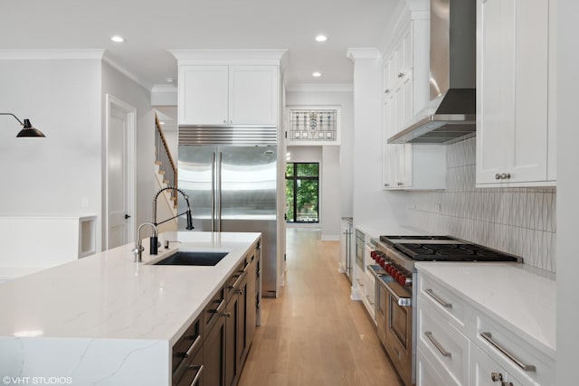 kitchen featuring crown molding, high end appliances, a sink, light wood-type flooring, and wall chimney exhaust hood