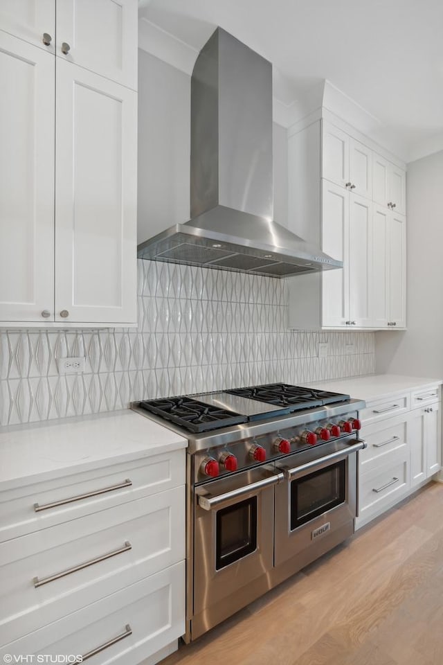 kitchen featuring light wood-style flooring, decorative backsplash, white cabinets, wall chimney range hood, and double oven range