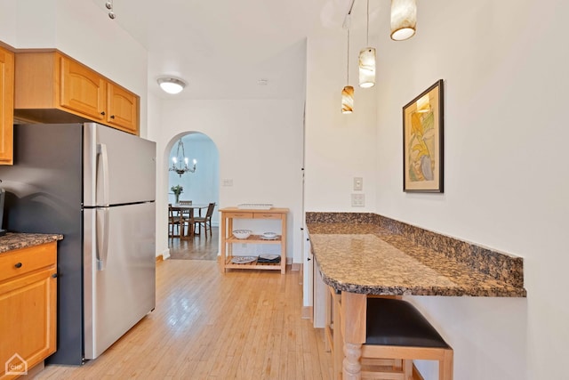 kitchen featuring arched walkways, a peninsula, a kitchen breakfast bar, freestanding refrigerator, and light wood finished floors