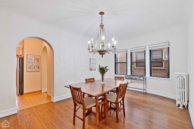 dining room with hardwood / wood-style flooring, radiator heating unit, arched walkways, and baseboards