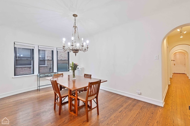 dining space featuring light wood-style floors, arched walkways, a chandelier, and baseboards