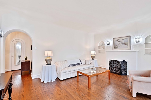 living room with arched walkways, built in shelves, hardwood / wood-style flooring, a fireplace, and baseboards