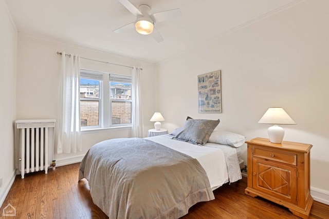 bedroom with radiator heating unit, wood-type flooring, a ceiling fan, and baseboards