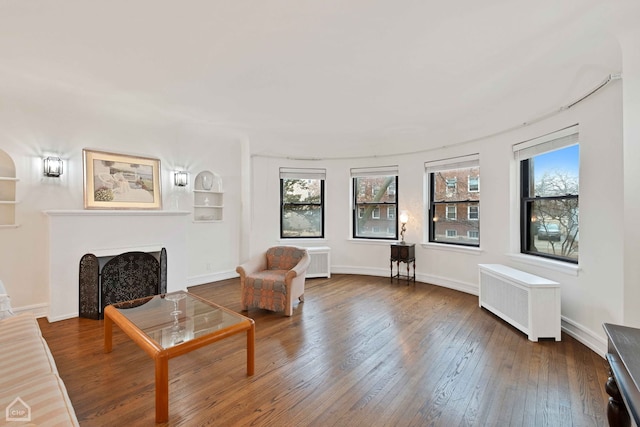 living area with radiator heating unit, a fireplace, baseboards, and hardwood / wood-style floors