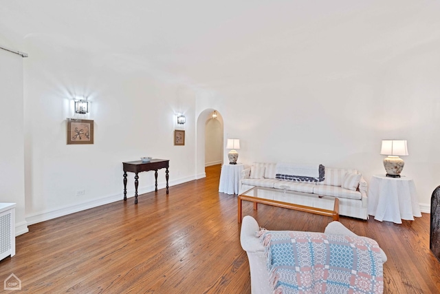 living room featuring arched walkways, wood finished floors, and baseboards