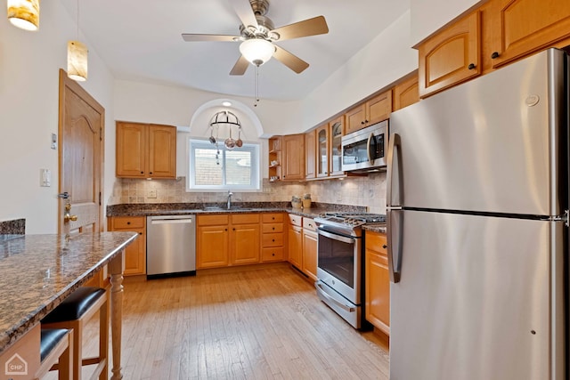 kitchen featuring appliances with stainless steel finishes, dark stone counters, light wood-type flooring, and tasteful backsplash