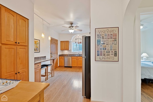 kitchen with arched walkways, backsplash, appliances with stainless steel finishes, light wood-style floors, and ceiling fan