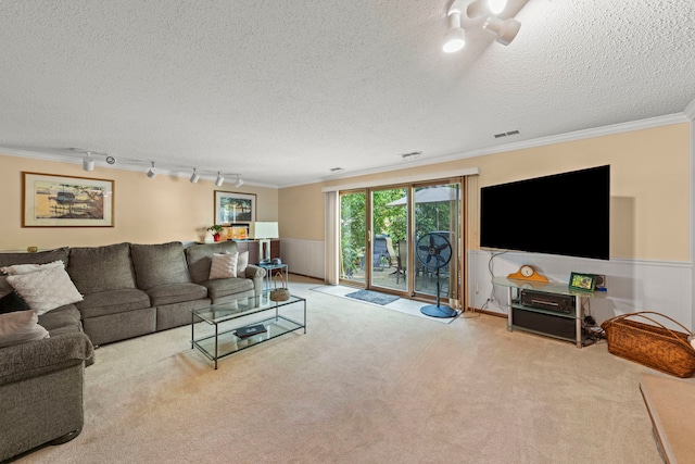 carpeted living area featuring visible vents, a wainscoted wall, ornamental molding, a textured ceiling, and track lighting