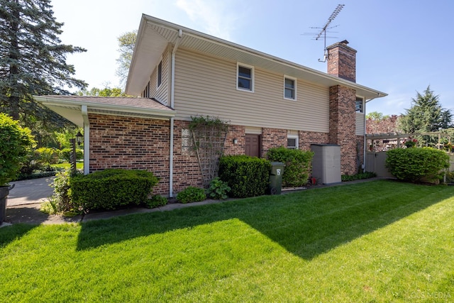 back of property featuring a chimney, a lawn, and brick siding