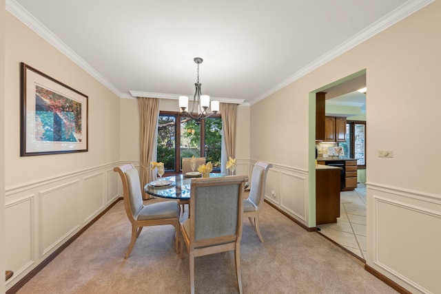 dining space featuring wainscoting, light colored carpet, ornamental molding, a chandelier, and a decorative wall