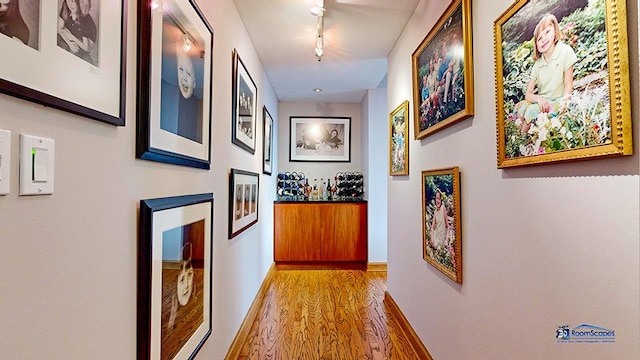 hallway featuring baseboards, track lighting, and wood finished floors