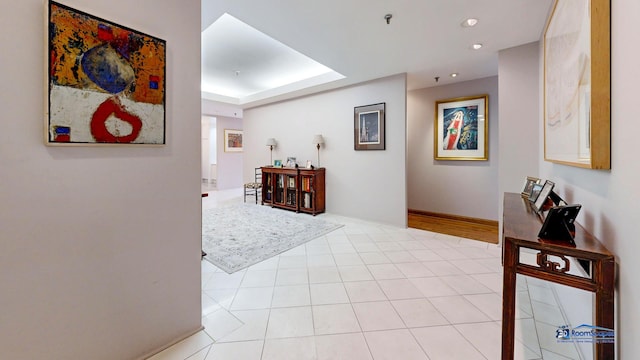 hall with recessed lighting, a tray ceiling, and tile patterned floors