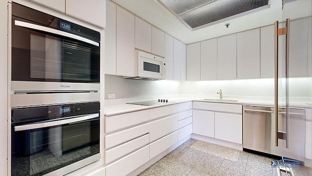 kitchen with stainless steel appliances, light countertops, granite finish floor, white cabinetry, and a sink