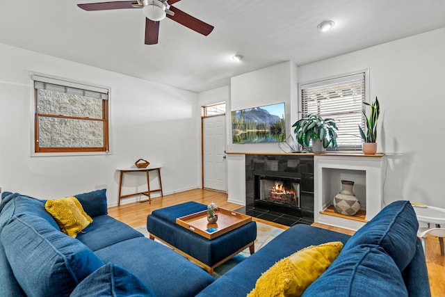 living room featuring a tiled fireplace, wood finished floors, baseboards, and a ceiling fan