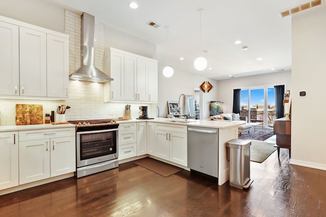 kitchen with stainless steel appliances, decorative backsplash, a sink, wall chimney range hood, and a peninsula