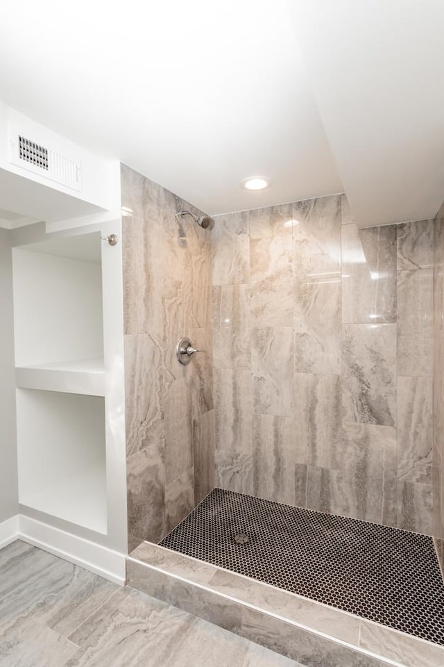 bathroom with a tile shower, visible vents, and baseboards