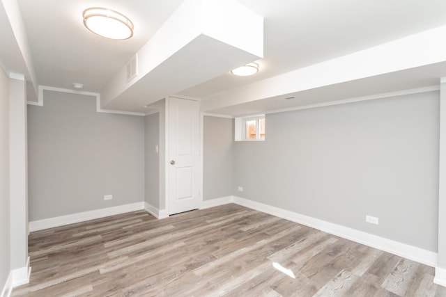 below grade area with baseboards, crown molding, visible vents, and light wood finished floors