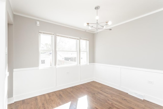 unfurnished room featuring visible vents, an inviting chandelier, ornamental molding, wainscoting, and wood finished floors