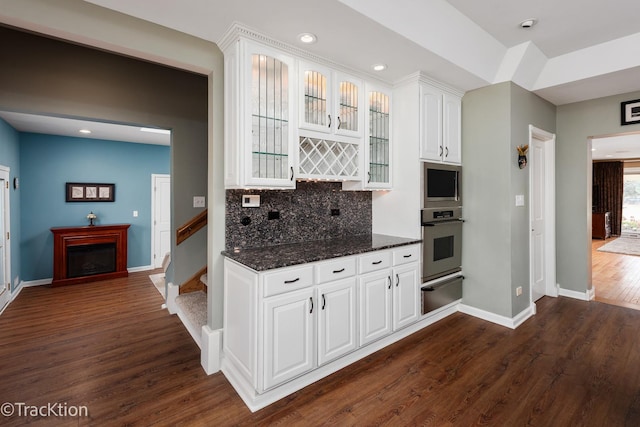 kitchen featuring glass insert cabinets, appliances with stainless steel finishes, white cabinetry, a warming drawer, and dark wood-style flooring