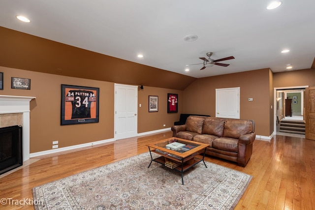 living area featuring a tiled fireplace, recessed lighting, light wood finished floors, baseboards, and vaulted ceiling