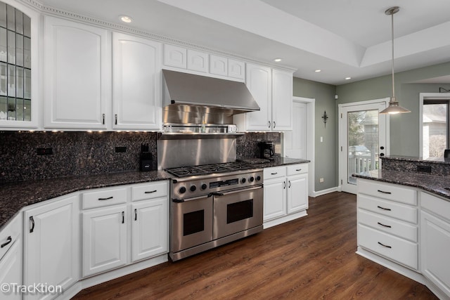 kitchen with dark wood-style floors, double oven range, dark stone counters, under cabinet range hood, and decorative light fixtures