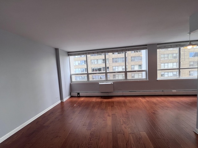 unfurnished room featuring dark wood-style floors, baseboard heating, and baseboards