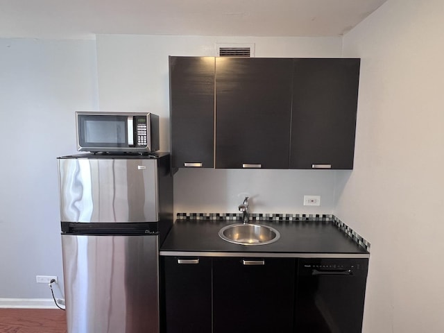 kitchen featuring appliances with stainless steel finishes, dark countertops, a sink, and dark cabinets