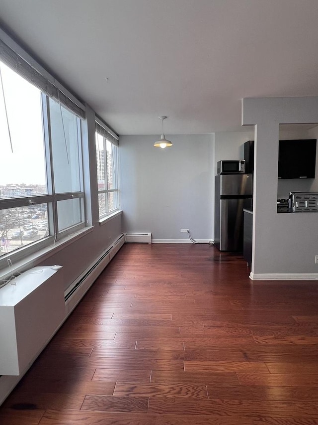 empty room featuring baseboard heating, baseboards, and dark wood finished floors