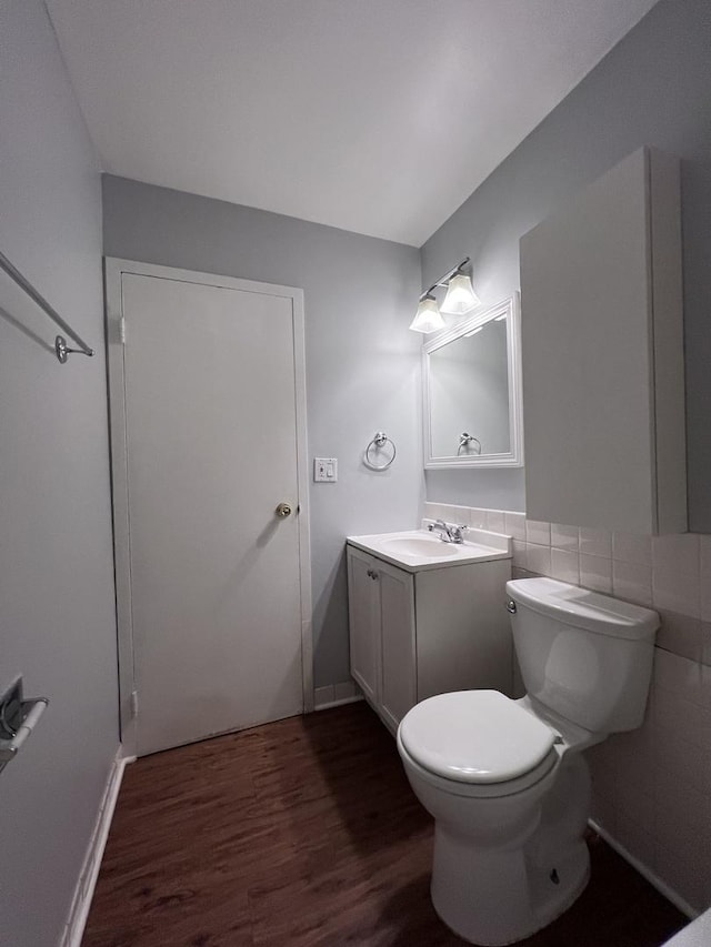 half bath featuring tile walls, vanity, toilet, and wood finished floors