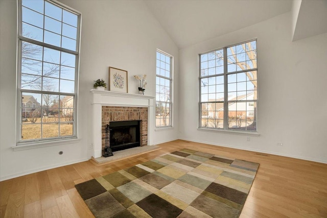 unfurnished living room with a fireplace, wood finished floors, baseboards, and high vaulted ceiling