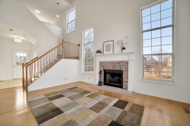 unfurnished living room with stairway, a brick fireplace, a towering ceiling, and wood finished floors