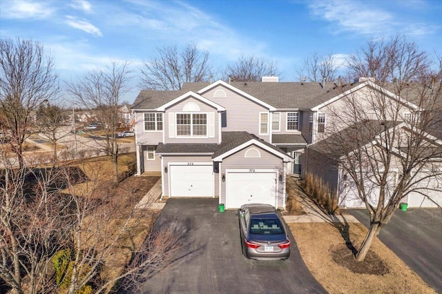 traditional home with aphalt driveway, a garage, a chimney, and a shingled roof