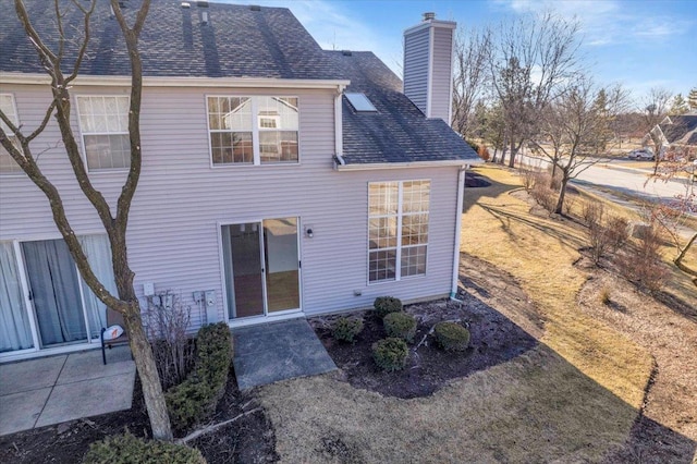 back of house with a chimney and a shingled roof