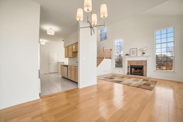 unfurnished living room featuring light wood-style floors, a high ceiling, a brick fireplace, a chandelier, and stairs