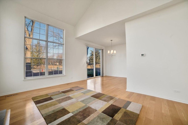 empty room featuring light wood-type flooring, visible vents, high vaulted ceiling, an inviting chandelier, and baseboards