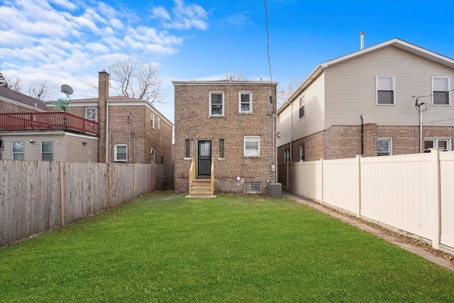 back of property with entry steps, a fenced backyard, a lawn, and brick siding