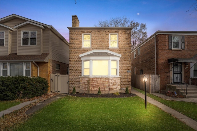 view of front facade with stone siding, a chimney, a gate, a front yard, and brick siding