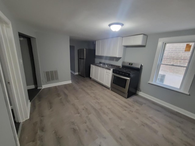 kitchen featuring freestanding refrigerator, white cabinets, stainless steel gas stove, and visible vents