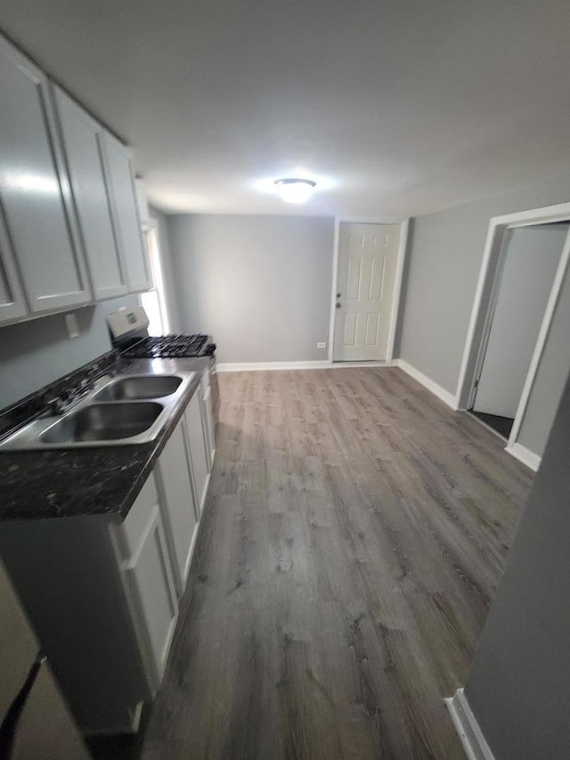 kitchen with white cabinetry, a sink, baseboards, and wood finished floors