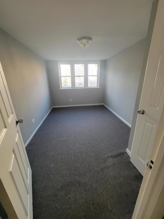 empty room with dark colored carpet and baseboards